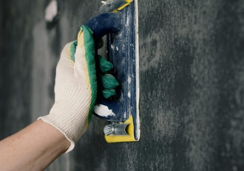 Crop anonymous male worker in gloves holding scraper and aligning walls in flat